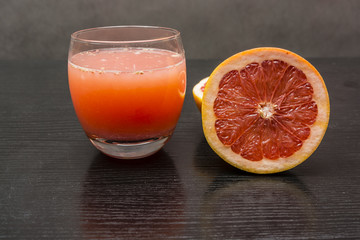 Freshly squeezed juice from pink grapefruits in a glass on a dark table.