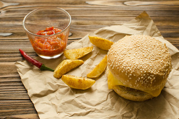 Cheeseburger with fried potatoes and chili  sauce on a  craft paper on wooden background with space for text