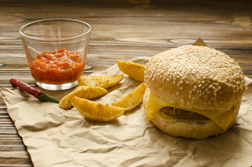 Cheeseburger with fried potatoes and chili  sauce on a  craft paper on wooden background with space for text