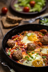 shakshuka, the Israeli dish of eggs, tomatoes and meatballs with greens on wooden background