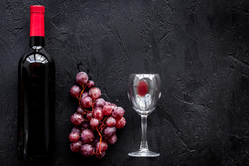 Taste red wine. Bottle of red wine, glass and red grape on black background top view copyspace