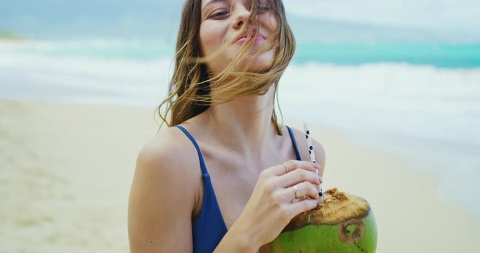 Beautiful young woman enjoying day at the beach drinking coconut