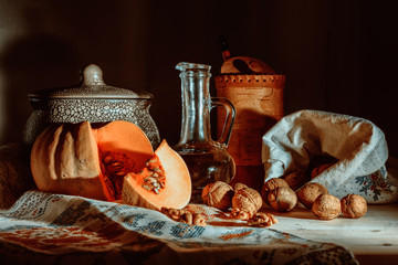 Rustic still life with pumpkin, walnuts, crockery and vegetable oil in a bottle on a dark background