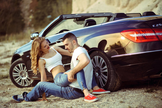 Man and woman hug each other and laughing sitting near in the Mercedes car. Passionate young couple. Вry desert terrain