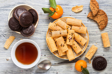 Waffles a straw in a plate with tea and chocolate biscuits on a wooden white table.