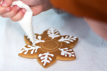 Child hands decorating gingerbread in the form of a a snowflake with icing sugar using a pipping bag. Christmas and New Year. Baking holiday cookies.