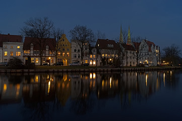 Obraz premium Row of houses with many lights on the riverbank with reflection at the blue hour