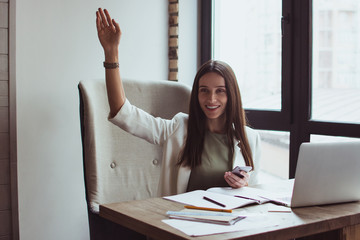 Hey there! Beautiful young businesswoman using her smart phone and gesturing with smile while sitting at her office desk