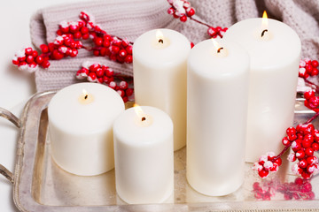White burning advent candles with red berries and cosy knitted blanket close up