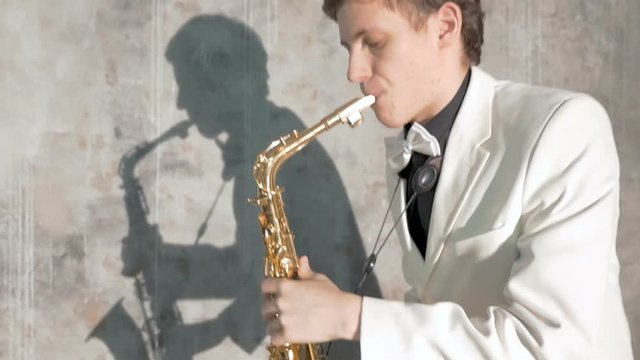 A musician in a white suit plays the saxophone. He performs in a nightclub, against a gray background. close-up