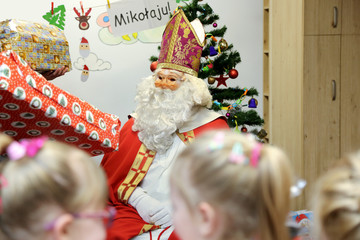 Święty Mikołaj rozdaje prezenty dzieciom w przedszkolu. - obrazy, fototapety, plakaty