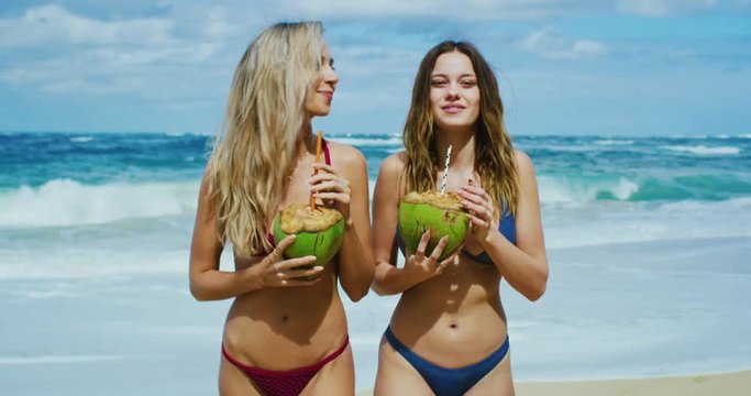 Beautiful girls walking on the beach drinking coconuts