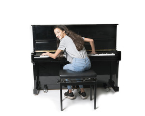 teenage brunette girl and black upright piano against white background in studio