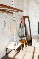 Corner of the loft design room with white brick walls, flowers in iron pot, mirror, coach. Boutique hanging rack concept