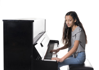 teenage brunette girl and black upright piano against white background in studio