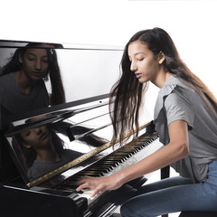 teenage brunette girl and black upright piano against white background in studio © ahavelaar