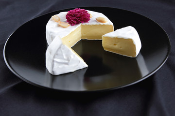 Cheese, camembert on a black plate, honey, pink flower, sliced cheese with mildew on a black velvet, minimalism, cheese on a black background, art