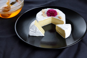 Cheese, camembert on a black plate, honey, pink flower, sliced cheese with mildew on a black velvet, minimalism, cheese on a black background, art