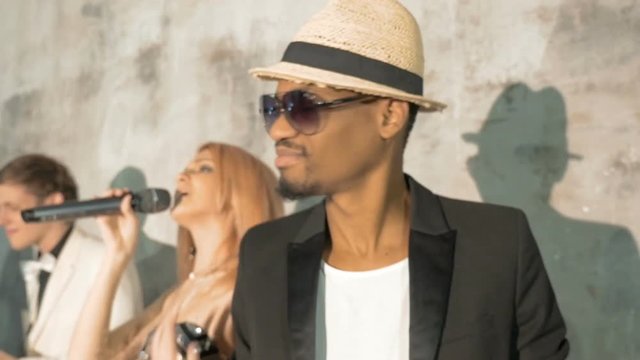 Four professional musicians dance and sing. Beautiful young blond woman and African man singing. The white musician plays the saxophone, an African man plays the drums.