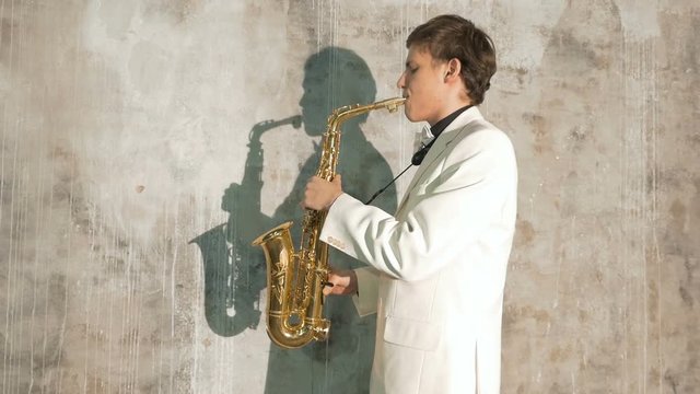 A musician in a white suit plays the saxophone. He performs in a nightclub, against a gray background. close-up