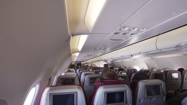 Aircraft cabin with rows of seats. Interior passengers airplane with people on seats. Passengers traveling by a modern commercial plane. Travel concept. 4K video.