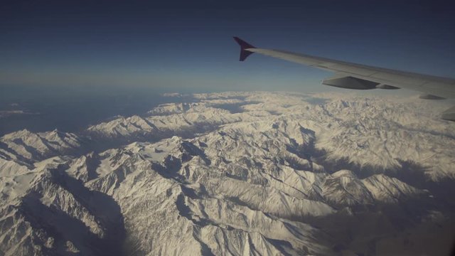 Mountain range with snow from the airplane window. Airplane wing. Aerial view on snowy mountains through window of an aircraft. Travel concept.