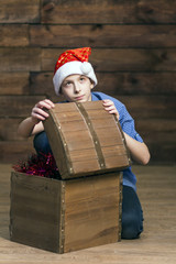 A Caucasian teenager is looking up thoughtfully when he opens a wooden chest with Christmas ornaments. Vertical photo.