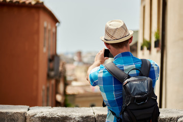 Male traveler in sunhat is taking a photo of a view with mobile phone.