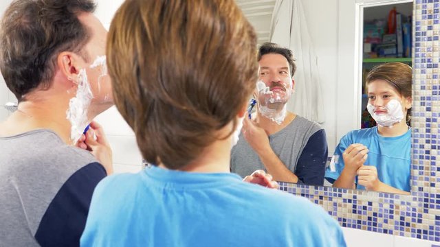 Cute boy with shaving cream in face making funny expressions with father in bathroom closeup