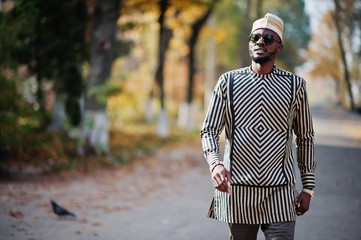 Portrait of stylish black african american man at hat and sunglasses against sunny autumn fall background. Rich people in africa at traditional dress.