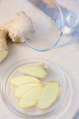 Slices of ginger root on glass plate over wooden board.