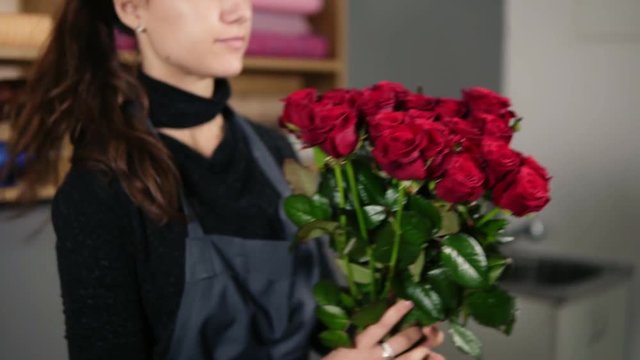Young attractive female florist arranging bouquet of beautiful red roses at flower shop. Slowmotion shot