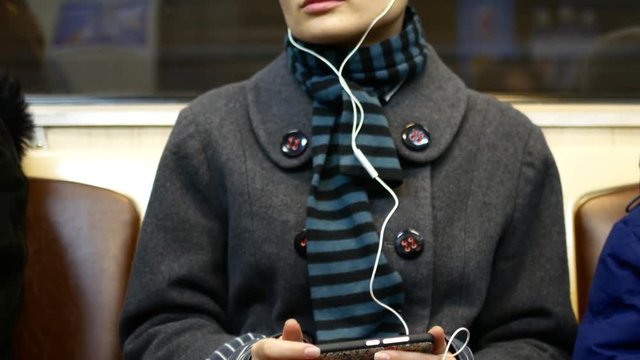 A girl listens to music or watches video on a smartphone in a subway car