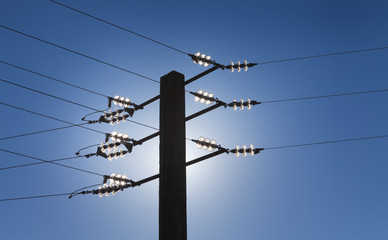 Electric power line against blue sky and backlit sun effect.