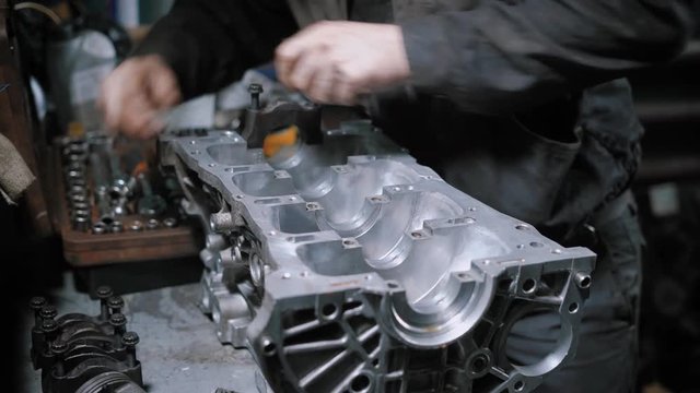 Close up shot of a professional mechanic disassembling engine block in car maintenance centre.
