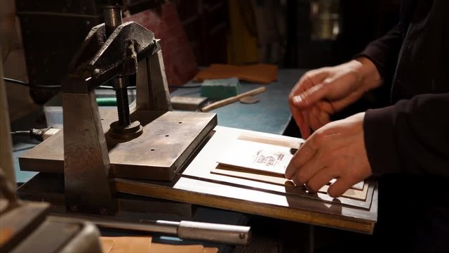 close up shot of a man's hands who works on industrial mechanical equipment, in his workshop he uses a press to create a logo on a piece of leather