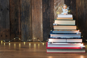 Christmas background with a pile of books, an angel, candles and a fir-tree garland