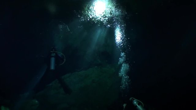Swimming with flashlight in dark caves of Yucatan cenotes underwater in Mexico. Natural landscape in clean and clear underground water. Unique scuba, diving