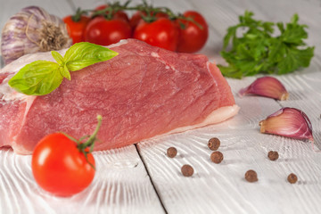 Meat with tomatoes and greens on a white wooden background