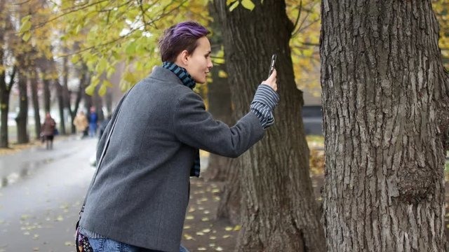 A woman is taking photos of trees and leaves on a mobile phone. Photo for social networks