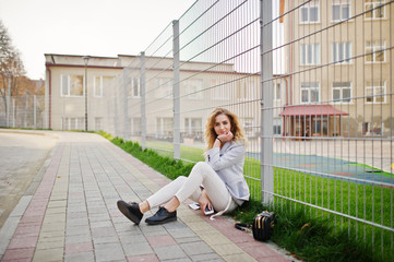 Stylish curly blonde model girl wear on white posing against fence.