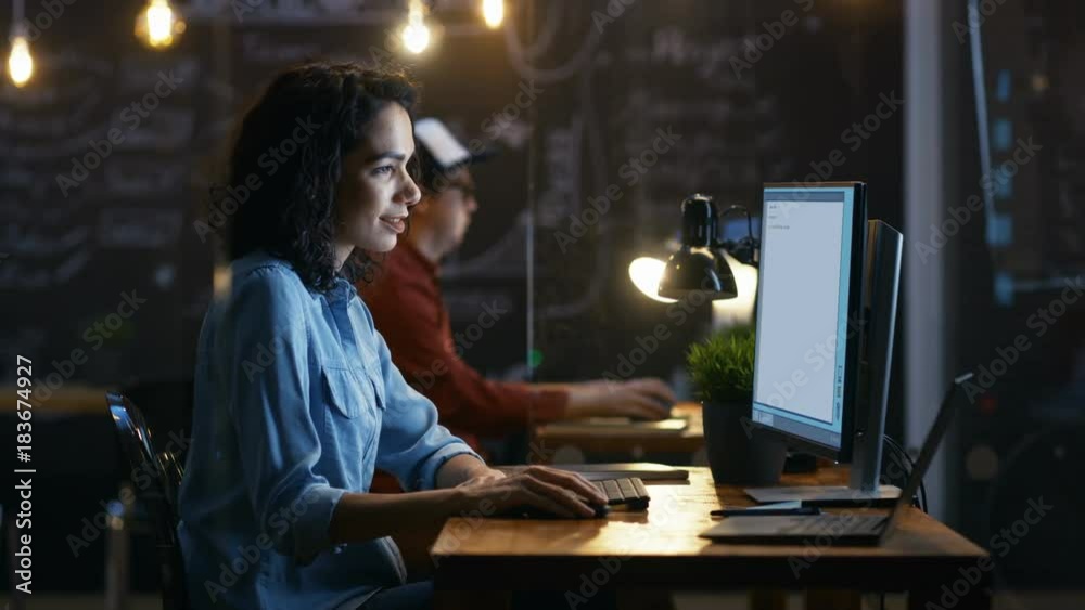 Poster beautiful female coder works at her desktop on her peropnal computer. her male colleague sits next t