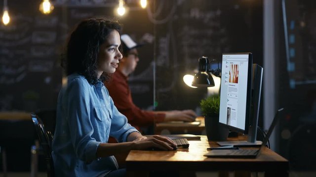Beautiful Female Office Worker Browsing Social Networks Site, Scrolling Web Page Wall. Her Colleague Sits in the Background in this Creative Office. RED EPIC-W 8K Camera.