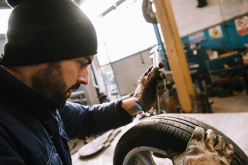 Mechanic, checking a measurement gauge to check the depth of a tread on a car tire for wear, to...