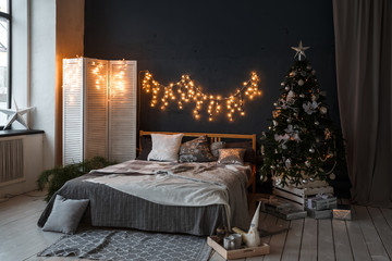 A spacious bedroom in a loft style with a decorated Christmas tree and a garland.