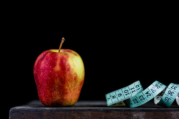 Tasty apple on an old dark wood table. Tape measure next to tasty fruit. Fruit on a diet.
