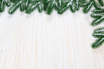 Christmas fir tree with snow on white wooden background. Free space frame