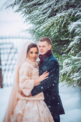Sensitive portrait of the cheerful beautiful newlywed couple. The groom is heating the hands of his charming brunette bride in the winter forest.