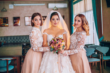 Fototapeta premium Happy beautiful bride with bridesmaids on wedding day, indoors. Girls with wedding flowers bouquet.