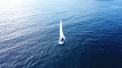 Aerial drone bird's eye view of yacht cruising near small islet of Ydrousa at sunset with beautiful scattered clouds, Voula, Athens riviera, Attica, Greece
